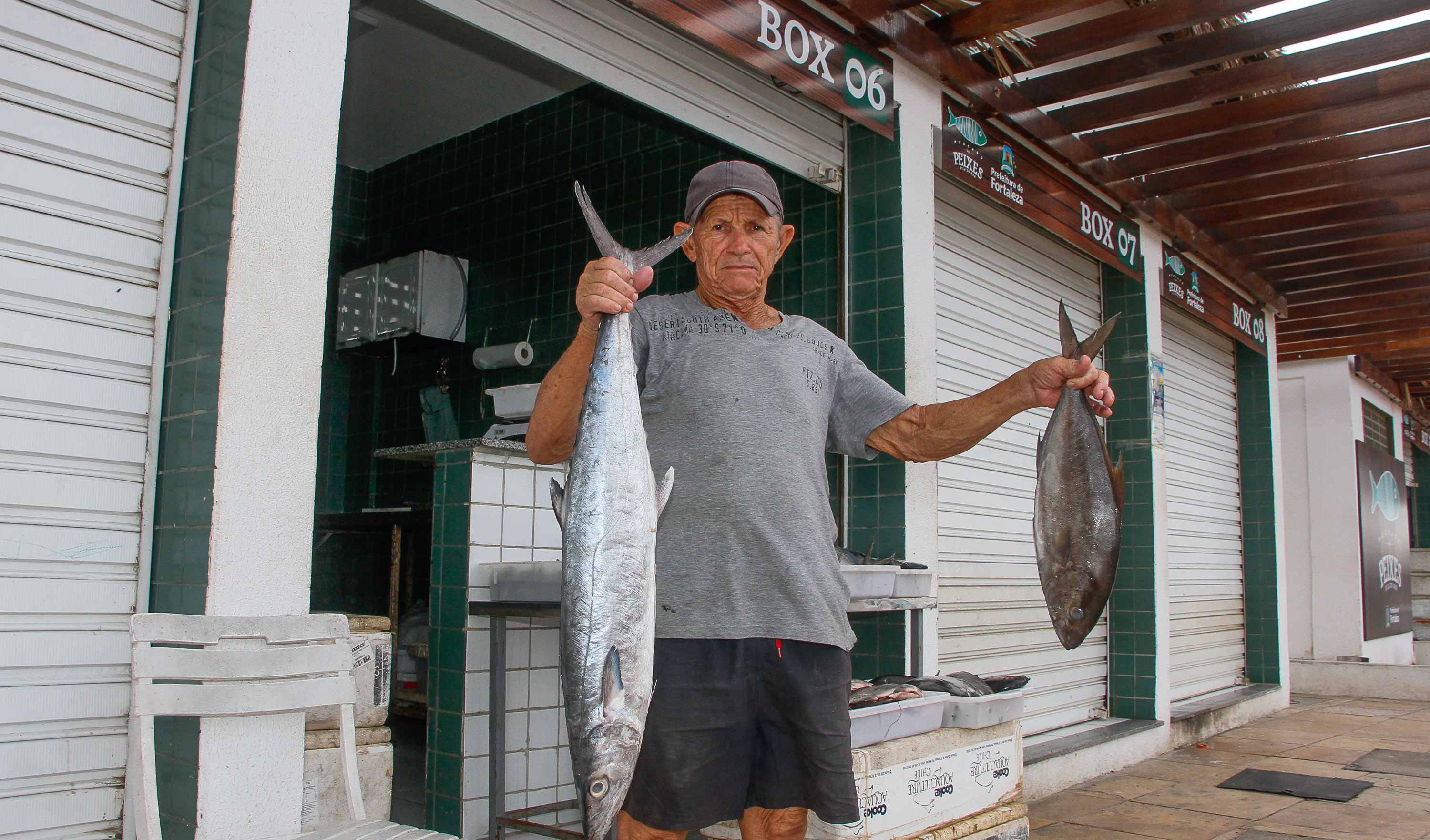 homem em pé posando para a foto e segurando um peixe em cada mão com mercado ao fundo
